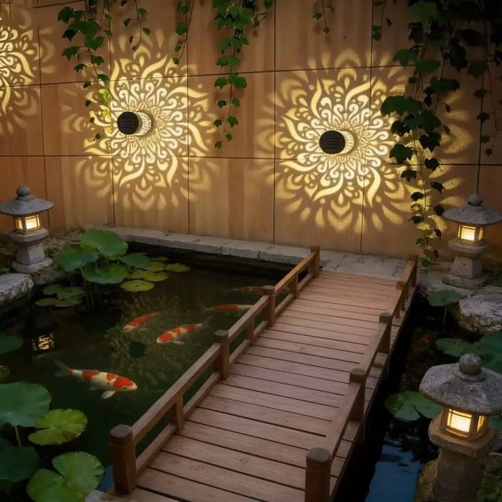 Outdoor garden scene with a pond, wooden walkway, and decorative wall lights casting patterns.