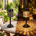 Two solar table lanterns with warm white light and decorative floral patterns on an outdoor patio table
