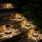 Two decorative outdoor lanterns with butterfly cutout patterns, casting warm light and shadow patterns on stone steps and foliage at night.