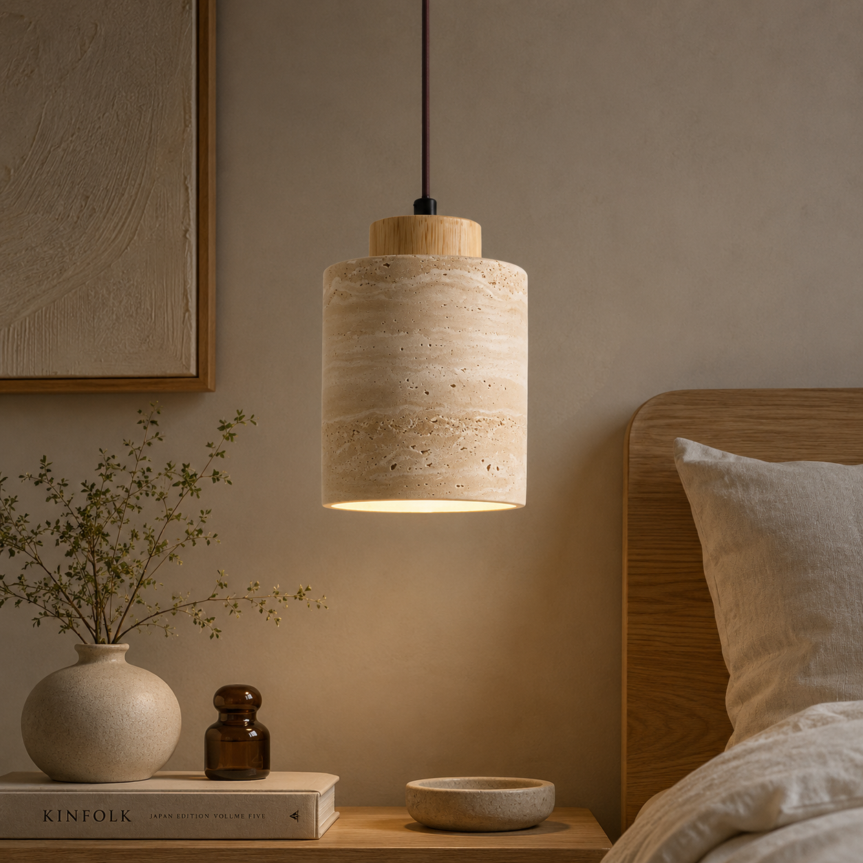 A cylindrical pendant light with a textured beige travertine stone shade and a natural wood top, hanging in a warm, modern bedroom setting next to a wooden headboard.